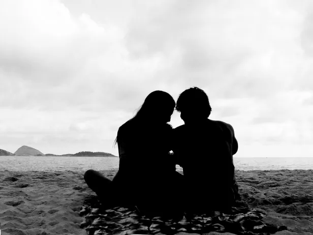 Silhueta em alto contraste de um casal sentado na areia da praia.