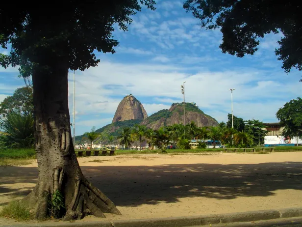Famoso morro com duas formações rochosas, visto por debaixo de uma árvore em uma área de areia.