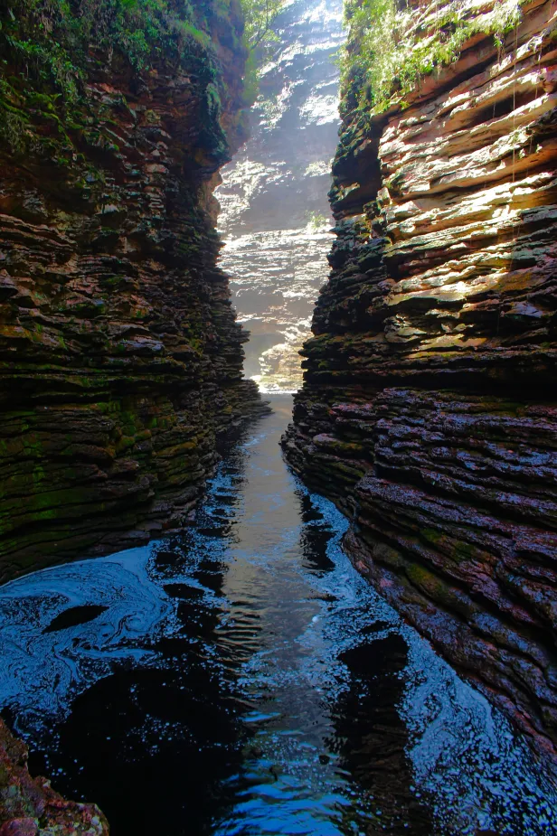 Rio com correnteza em meio a dois paredões de pedras dispostas em camadas.